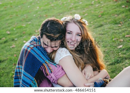 A picture of a young man covered his girlfriend with blanket in the park.