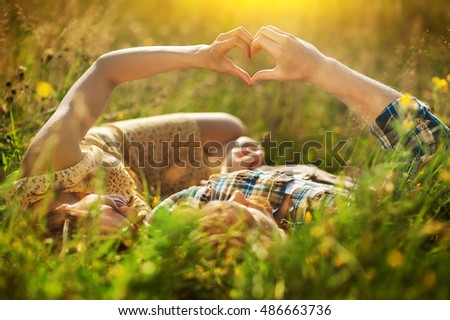couple of woman and man  lies on a flower meadow and holding hands in shape of heart