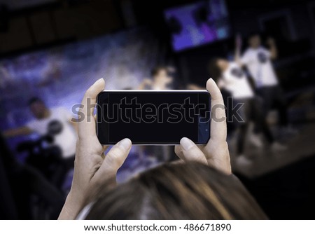Woman hand holding contemporary modern smartphone.Blurry people on fashion stage. Blank display replaceable with needed design.Horizontal mockup