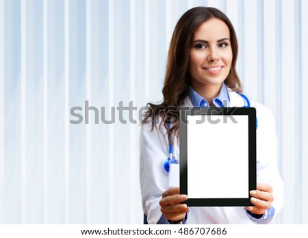 Portrait of happy smiling young female doctor showing no-name tablet pc with blank copyspace area for slogan or text, at office. Selective focus on tablet pc.