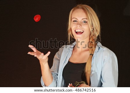 A beautiful young woman tosses a tomato in the air.