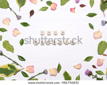 The phrase "good morning" on cubes in a frame of flowers, petals and green leaves on a white background.Inspirational image.Type flat, top view