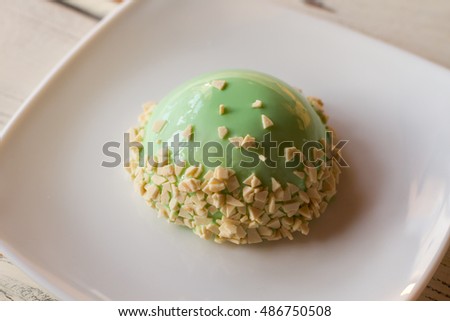 Sweet dish with green icing. Glazed dome cake on plate. Delicacy with mint mousse. Plain design of confectionery.