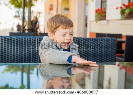 Emotional boy at a table in a cafe. Cute little boy sitting in outdoor restaurant on summer day. child in a cafe waiting for his order. 