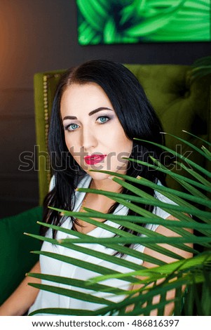 Beautiful brunette girl with blue eyes sits in green chair on background of the stylish room and picture