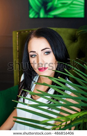 Beautiful brunette girl with blue eyes sits in green chair on background of the stylish room and picture