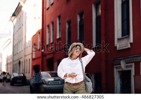 Young pretty hipster cheerful girl posing on the street at sunny day, having fun alone, stylish vintage clothes hat. Travel concept