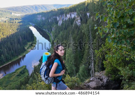 Young happy woman with backpack standing on cliff smiling and looking at camera