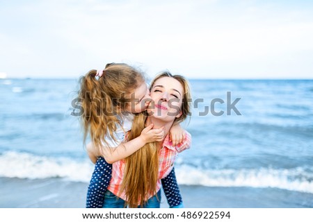 Beautiful young blonde mother and little cute girl kisses and laughs at the beach. Travel and Vacations.