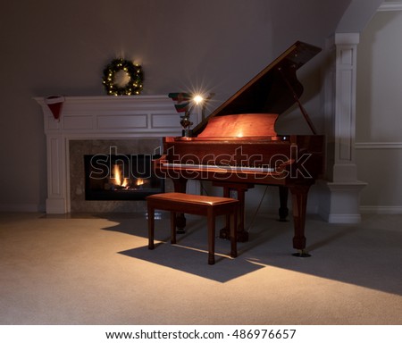 Piano with reading light on with glowing fireplace and Christmas decorations in background. Select focus on front of piano. 