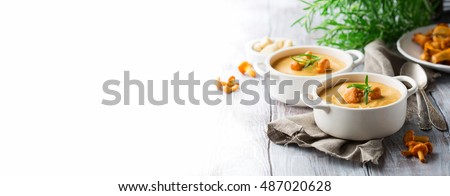 Mushroom cream soup with fresh chanterelles and herbs on a white rustic wooden background, selective focus. Autumn concept. Long web format