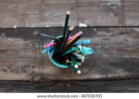 Stack of colored pencils in a glass on wooden background,top view.