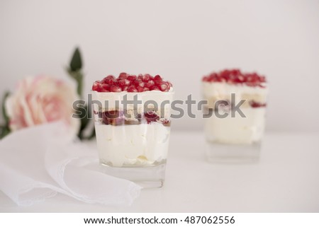 Homemade layered dessert with mascarpone, chocolate, cream, fresh strawberries, cookies, pomegranate. Cheese in a glass. White background, high key, selective focus