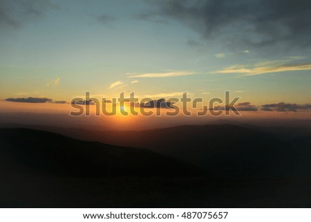 beautiful view on sunset or sunrise in blue sky with clouds and yellow orange sun in mountains on natural background