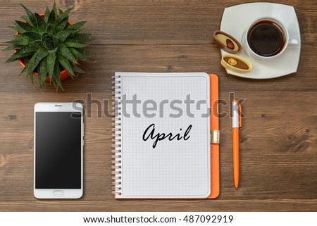 Composition of Title of month name April and Business (school) accessories (notebook, diary, mobile phone, cactus, pens, pencils), a cup of coffee on a wooden table. Top view.