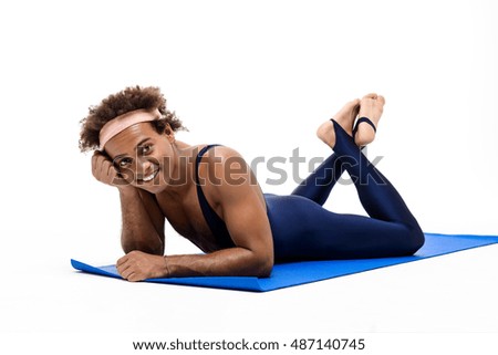 Sportive african man smiling, lying on karemat over white background.