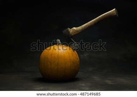Halloween-pumpkin with an Axe sticking in it. Dark background an setting.
