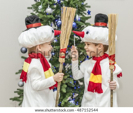 Boys, twins in carnival costumes of snowmen. Stand hold hands before the Christmas fir-tree.