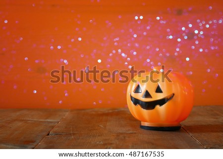 Halloween holiday concept. Cute pumpkin on wooden table and glitter lights overlay