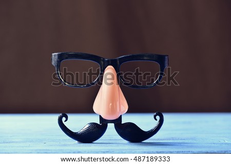 closeup of a fake mustache, nose and eyeglasses on a rustic blue wooden surface Royalty-Free Stock Photo #487189333