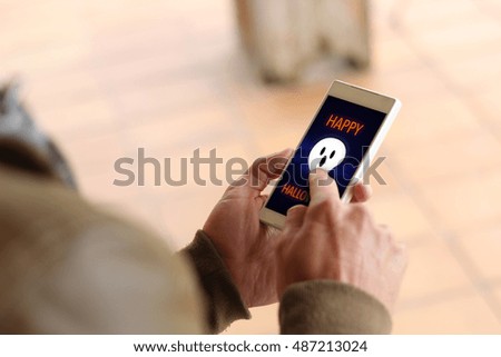 lifestyle concept: Hands male with a digital card Halloween on smartphone. All graphics on the screen are made up.