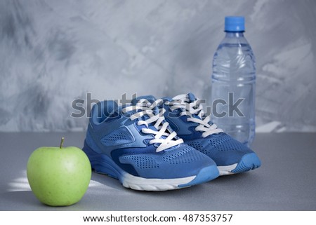 Sport shoes, apple, bottle of water on gray concrete background. Concept healthy lifestyle, sport and diet. Sport equipment. Focus is only on the sneakers.