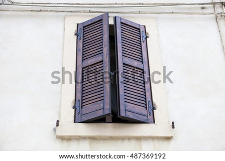 Old window with closed shutters with flowers on the window sill on the stone wall. Italian Village.