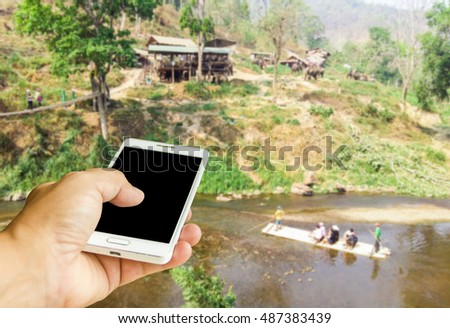 Man use mobile phone, blur image of rafting in Thailand as background.