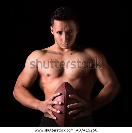 Football player with ball in his hands in black background. Tattoo says No pain No victory / Football player holding a ball in his hands