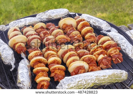 Close up picture of meat skewers with onions and corn cobs in aluminum foil, garden barbecue, selective focus.