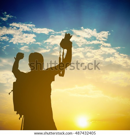 Silhouette of happy backpacker photographer during in sunset sky