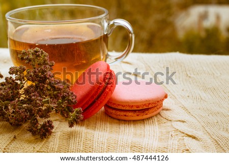 Fresh colorful macaroons with a cup of tea on warm knitted sweater, close up selective focus toned image. Lifestyle background.