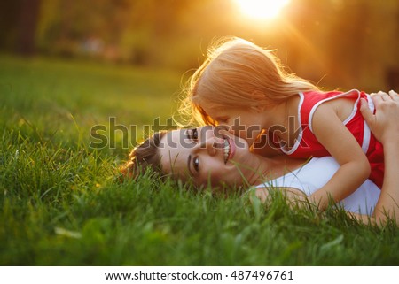 Mother and daughter lying on the lawn. Daughter kiss her mother on the cheek. Family in the city park outdoors. Happiness of motherhood and childhood.