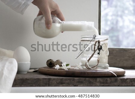 rustic still life. female hand is pouring milk in a glass jar vintage. fresh milk and eggs against a rustic background. Milk is in a vintage glass milk bottle.