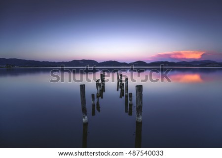 Wooden pier or jetty remains on blue lake sunset and sky reflection water. Long exposure, Versilia Massaciuccoli, Tuscany, Italy.