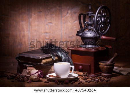 Cup of coffee, dry rose, old books, crow quills and coffee grinder on wooden table. Vintage still life.