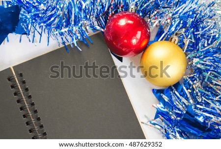 Christmas or New year flat composition. Blue sparkling ribbon wreath. Fir tree toys. Black paper note pad with blank page. Seasonal decor mockup for greeting message or lettering. Festive background