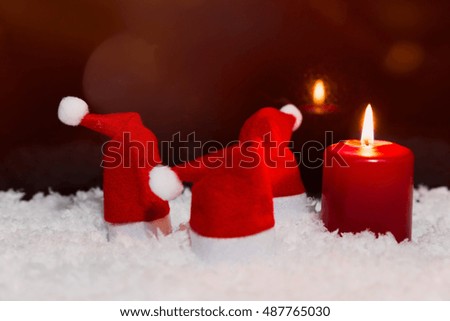 Red pointed hats and candle in the snow, red background, copyspace