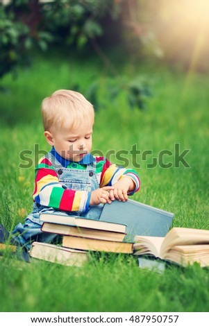 one year old baby reading a book sitting on the grass in garden
