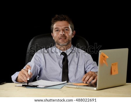 corporate portrait of happy successful businessman in shirt and tie smiling at office desk working with laptop computer isolated on black background confident and trustful in business success concept