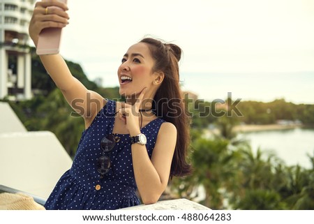Teenager asian girl waving to the camera during a smart phone video call in vacations with the sea in the background