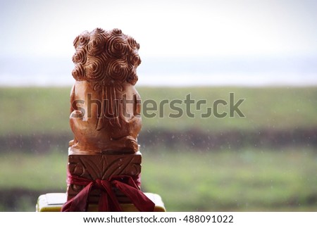 Back shot of a golden lion statue as a guardian of a Buddhist temple in Indonesia, facing outside landscape view on a rainy day