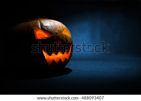 The carved face of pumpkin glowing on Halloween on blue background