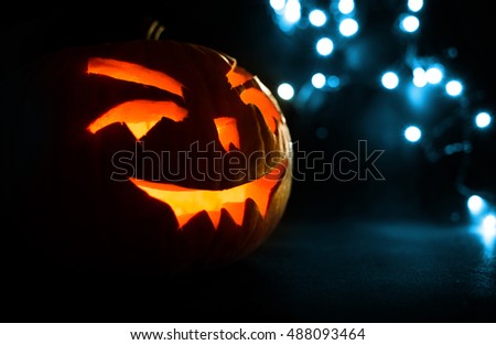 carved face of pumpkin glowing on Halloween on blue bokeh light background