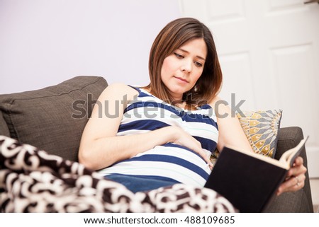 Beautiful young expectant mother relaxing at home and reading a book while waiting for her due date