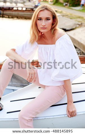 model tests of fashion blond girl in shirt posing in the boat in the dock by the sea