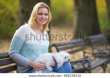 Beautiful young woman with little dog sitting on bench and smiling