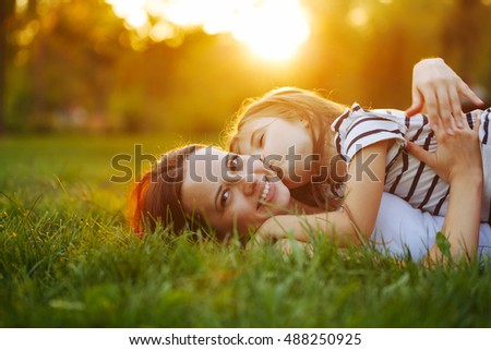 Mother and daughter lying on the lawn. Daughter kiss her mother on the cheek. Family in the city park outdoors. Happiness of motherhood and childhood. On the Sunset