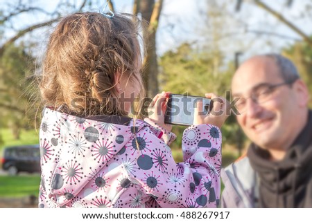 young happy man having fun with his little cute blond daughter taking selfie photo with mobile phone enjoying together outdoor in park