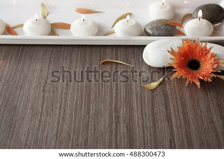 Spa stones with candles, flower and petals on wooden background